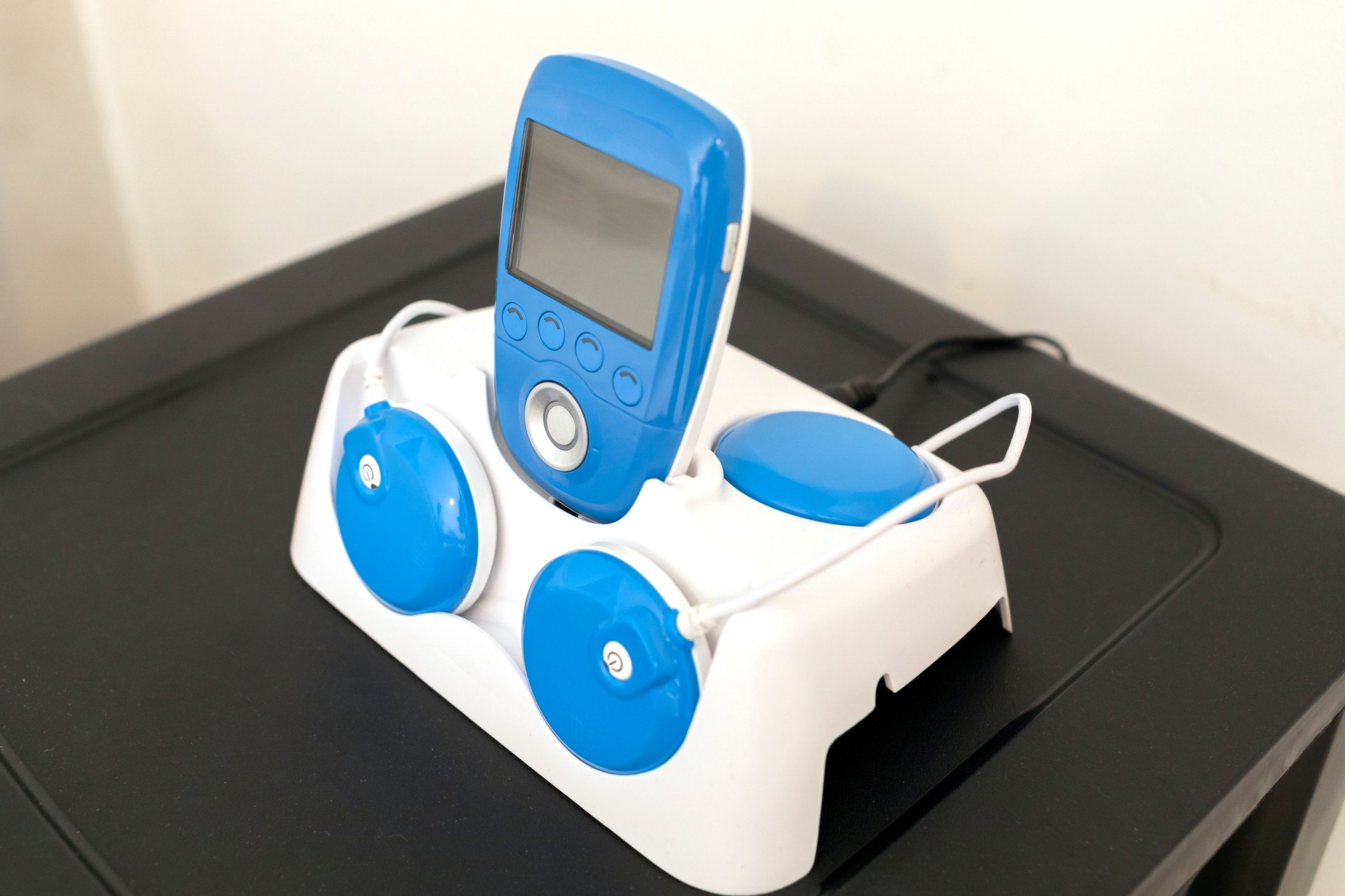 Closeup Blue Wireless Electric Muscle Stimulator, Pain Treatment on Shelf. Charging Rehabilitation and Training Tool, Equipment. Healthcare and Medical concept. Horizontal plane.